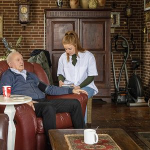 Assisted living nurse taking elderly mans blood pressure with mobile medical device